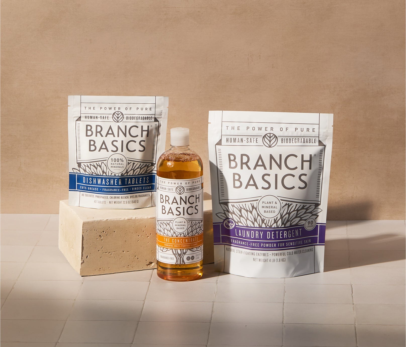A bottle of Branch Basics Concentrate, a pouch of Dishwasher Tablets, and a pouch of Laundry Detergent are displayed on tiled surface and neutral background. - View 1
