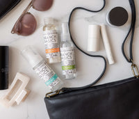 The Travel Kit, featuring mini-versions of the Branch Basics Concentrate, All-Purpose spray, and Foaming Wash pump, displayed on a neutral background, spilling-out from a purse. - Thumbnail View 3
