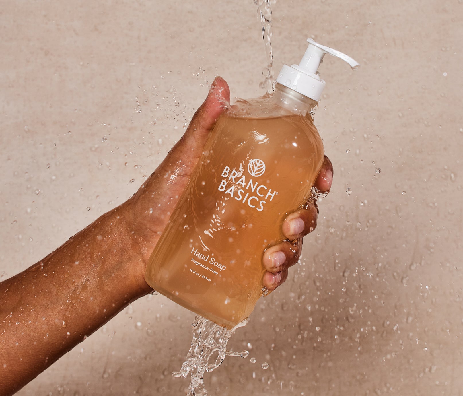 A glass bottle of Branch Basics Gel Hand soap, displayed in a person's hand, set against a neutral background. - View 1
