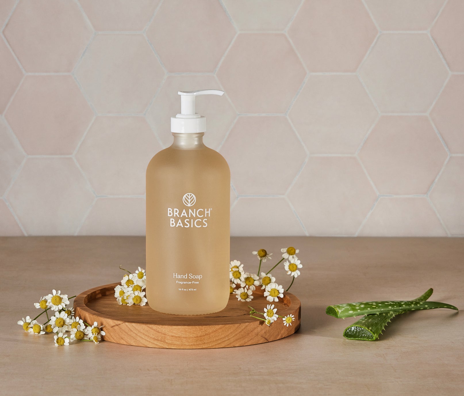 A glass bottle of Branch Basics Gel Hand soap, displayed on a wooden tray with a neutral tiled background. - View 3
