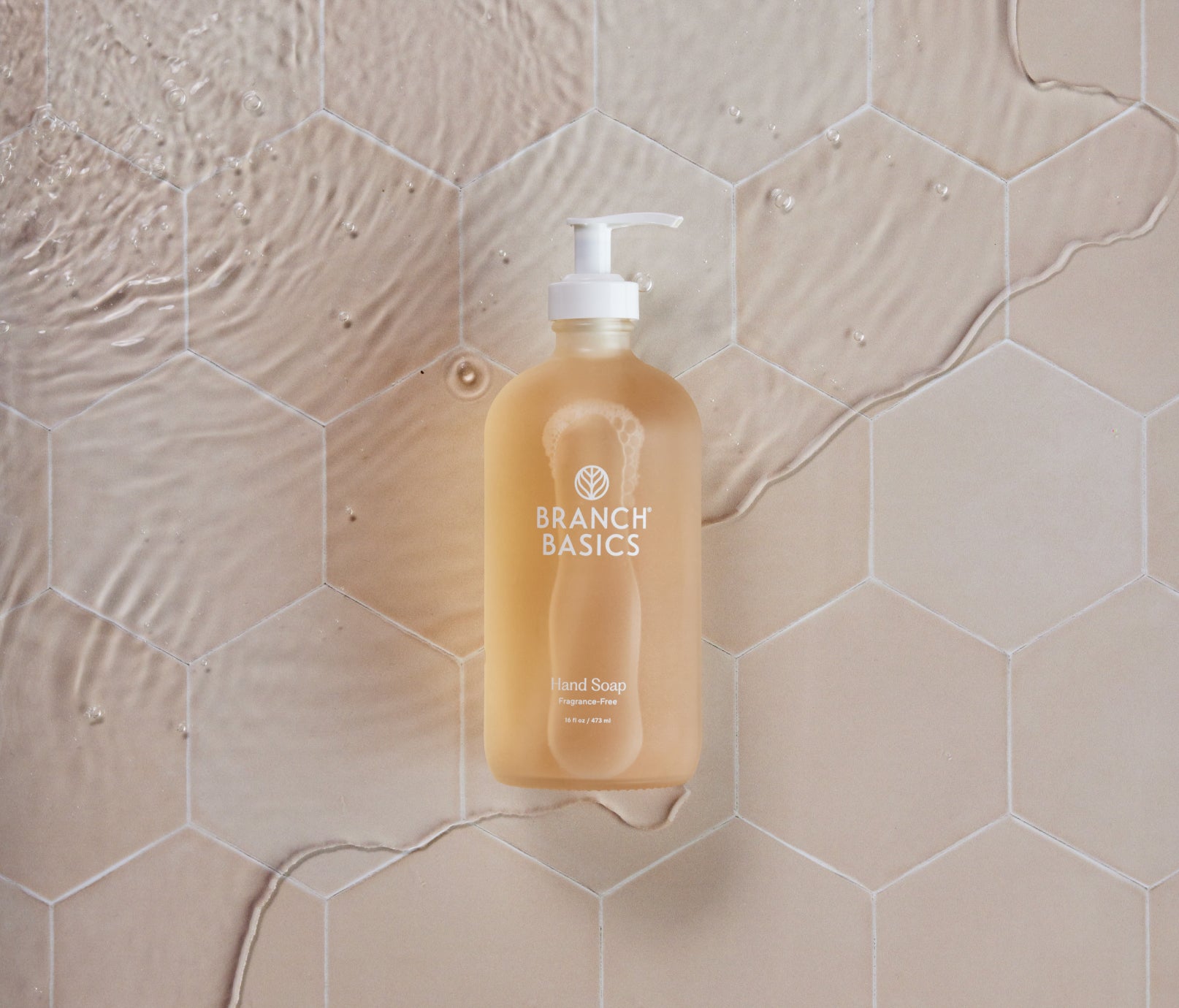 A glass bottle of Branch Basics Gel Hand soap, displayed on a neutral tiled background. - View 4
