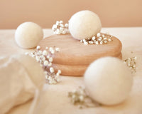 Multiple Wool Dryer Balls are pictured, with the two in the foreground out of focus, the one in the background partially-in-focus, and the one in the midground in-focus and elevated on a wooden tray. - Thumbnail View 3
