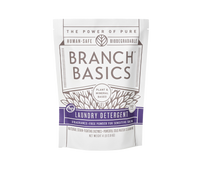 A pouch of Branch Basics Laundry Detergent powder. The packaging is white with purple and grey accents and text that highlights the product features, including 'plant-based formula' and 'human-safe, biodegradable'. - Thumbnail View 1
