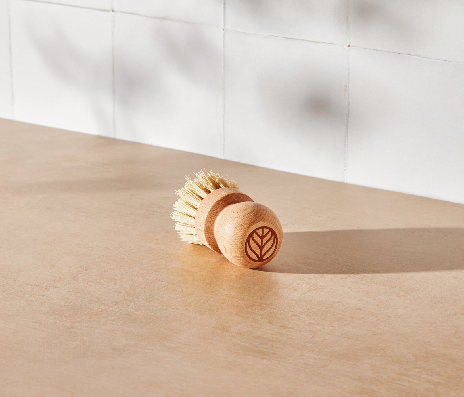 A Natural Scrub Brush, made with a solid beechwood handle and natural fiber bristles, displayed on a neutral surface and white tiled background. - View 1
