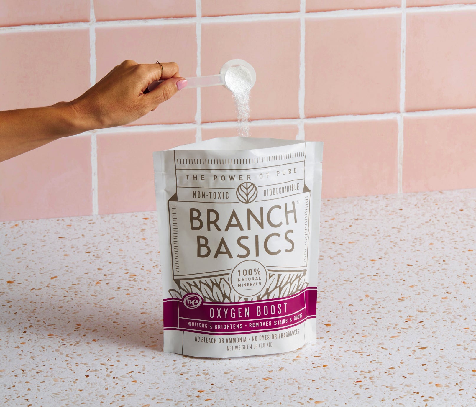 An open pouch of Branch Basics Oxygen Boost; a person is pouring a scoop of the white, granular product back into the original container. - View 1
