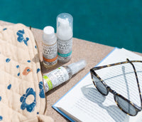 The Travel Kit, featuring mini-versions of the Branch Basics Concentrate, All-Purpose spray, and Foaming Wash pump, displayed poolside, next to an open book and sunglasses. - Thumbnail View 4
