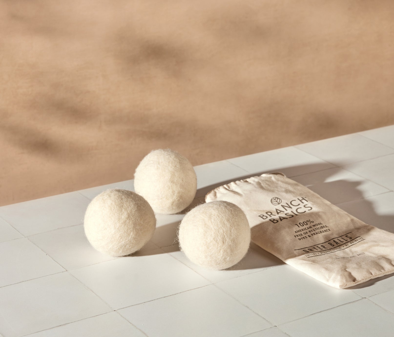 A trio of Wool Dryer Balls accompanied by a cloth carrying bag, displayed on a white tiled surface and neutral background. - View 1

