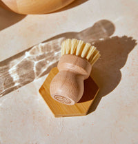A Natural Scrub Brush, made with a solid beechwood handle and natural fiber bristles, displayed on an elevated wooden tray and neutral background. - Thumbnail View 3
