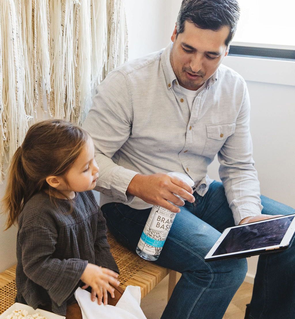 An adult and child sitting together on a bench, using a Plastic Streak-Free bottle to clean fingerprints from the glass screen of a tablet device. - View 3
